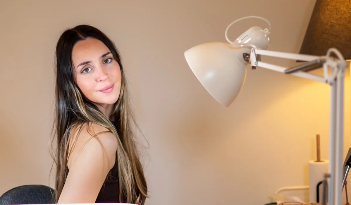 אישה יושבת בעמדת העבודה בסטודיו, מנורת זרוע לבנה לצידה