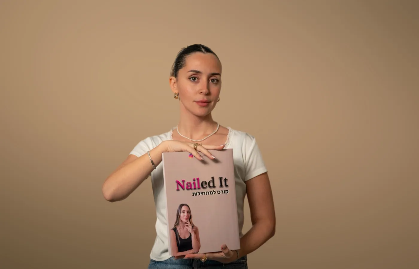 אישה מחזיקה חוברת קורס מודפסת עם הכיתוב Nailed It על רקע חום בהיר