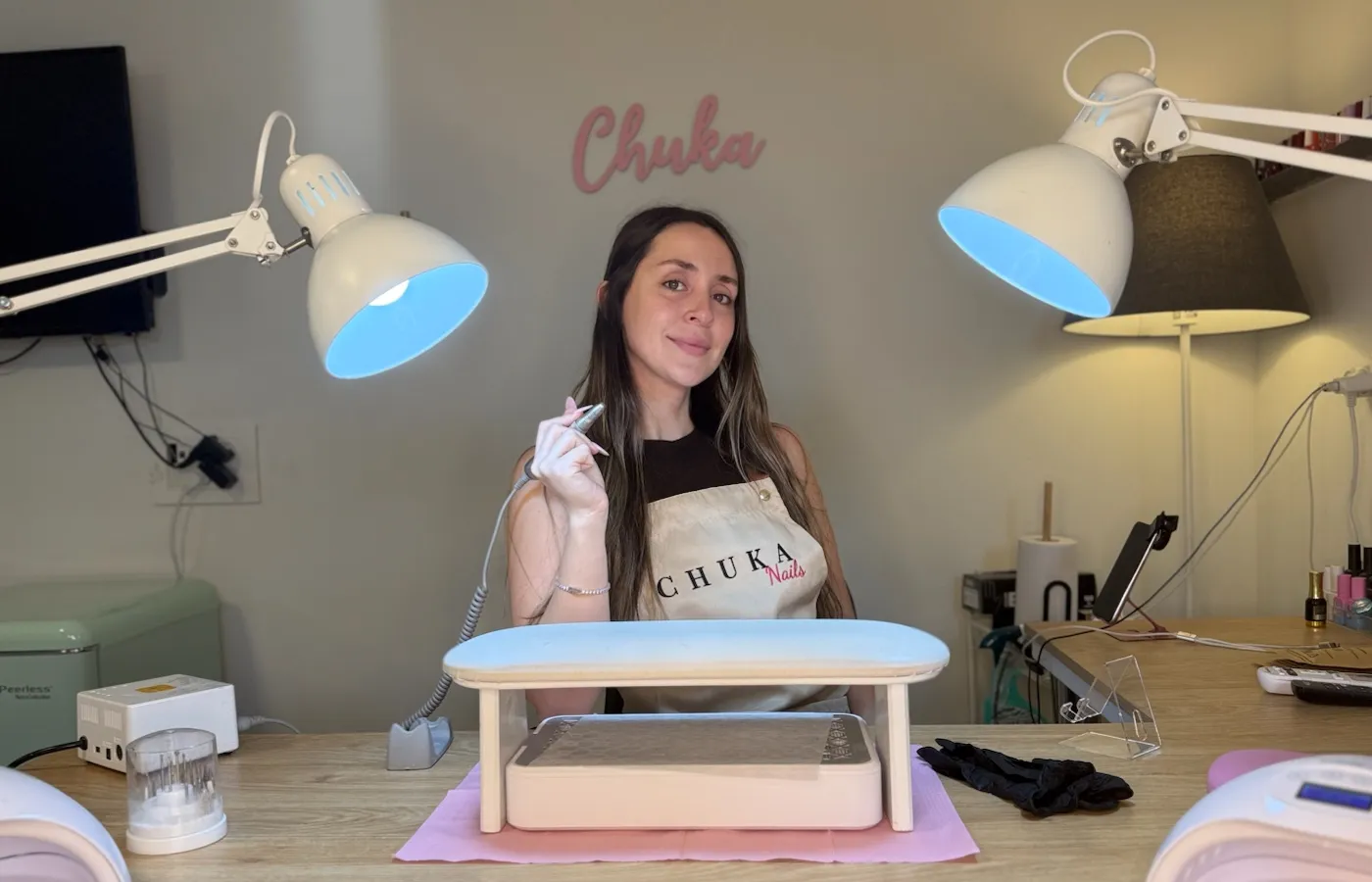 מטפלת בסינר Chuka Nails בעמדת העבודה בסטודיו, עם משענת יד ומנורות